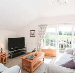 A living room with a sofa a coffee table and a television near a balcony door at The Cider Shed in Winscombe