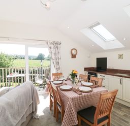 A dining area with a table set for six and a kitchen with white cabinets and skylights at The Cider Shed in Winscombe