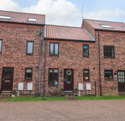 A brick townhouses facade with multiple windows and doors and a gravel driveway at Maplebeck in Whitby