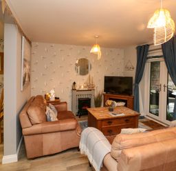 A living room with two brown sofas a wooden coffee table a TV on a wooden stand and blue curtains at Maplebeck in Whitby