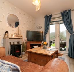 A living room with brown leather sofas a wooden coffee table and a television near blue curtains and a fireplace at Maplebeck in Whitby