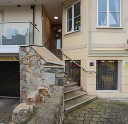 Exterior view of a building entrance with stone wall stairs leading up to a door and a balcony with chairs above a garage at Puffin View in Rhos-On-Sea