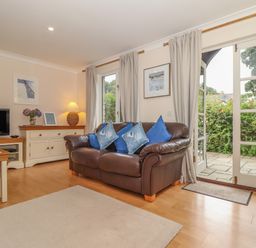 A living room with a leather sofa and blue cushions next to a glass door leading outside at Deja Blue in Falmouth