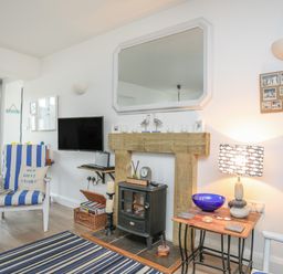 A living room with a striped chair a wood stove and a TV on the wall at The Old Boat Store in Morfa Nefyn