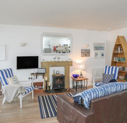A living room with striped chairs a wooden shelf shaped like a boat and a wall-mounted television at The Old Boat Store in Morfa Nefyn