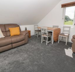 A sitting room with two brown sofas a wooden dining table with four chairs and a window showing a grassy field at Little Valley View in Angarrack