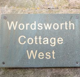 A metal sign with the text Wordsworth Cottage West mounted on a stone wall at Wordsworth Cottage West Longframlington