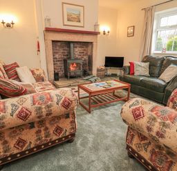 A living room with patterned sofas a leather sofa a wood burning stove and a coffee table at Wordsworth Cottage West in Longframlington