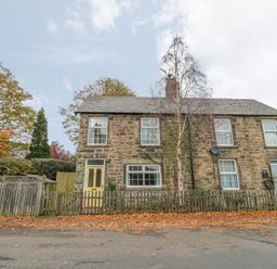 A stone cottage with yellow and blue doors and a wooden fence in front at Wordsworth Cottage West in Longframlington