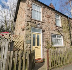 A stone exterior of a cottage with a yellow front door and wooden fence at Wordsworth Cottage West in Longframlington