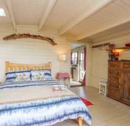 A bedroom with a wooden bed blue and white bedding a wooden dresser and a chair at Songbird Hideaway in Pwllheli