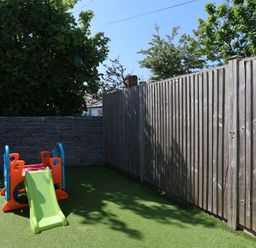 A small playground with a plastic slide on artificial grass surrounded by wooden and stone fences at Rosebank Cottage in Mortehoe