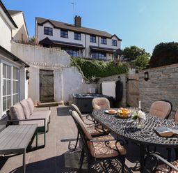 An outdoor patio area with a dining table and chairs a sofa a coffee table and a hot tub at Rosebank Cottage in Mortehoe