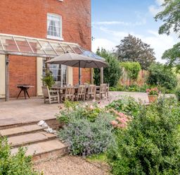 An outdoor patio with a dining table and chairs under an umbrella next to a brick building and garden at Hilltop House in Tenbury Wells