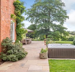 An outdoor patio with a hot tub wooden dining table chairs umbrella and large tree at Hilltop House in Tenbury Wells