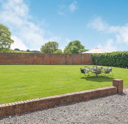 A garden with a lawn table set and umbrella surrounded by brick walls and hedges at The Chestnuts in Tenbury Wells