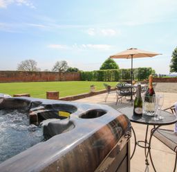 An outdoor patio with a hot tub a table with champagne bottles and glasses and a seating area with umbrella at The Chestnuts in Tenbury Wells
