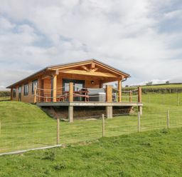 A wooden cabin with a covered porch and outdoor furniture on a grassy hill at Bryn Eiddon Log Cabin in Machynlleth