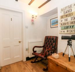 A room with a wooden rocking chair a telescope on a wooden chest and a sign on the wall at Tyddyn Serri in Rhosneigr