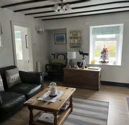 A living room with a sofa, coffee table, and armchair at Tyddyn Serri in Rhosneigr