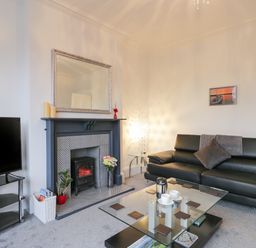 A living room with a black leather sofa, glass coffee table, electric fireplace, flat screen TV, and a floor lamp at Beach House in Bridlington