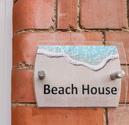 A glass sign with a beach design and the text Beach House mounted on a red brick wall at Beach House in Bridlington