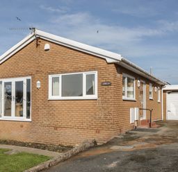 A brick house with white windows and a driveway leading to a garage at Arwelfa in Penmaenmawr