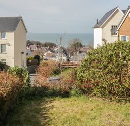 A garden with bushes and grass between two houses with a sea view at Arwelfa in Penmaenmawr