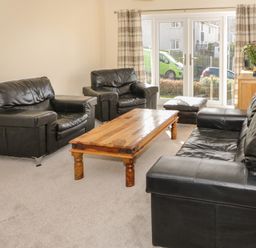 A living room with black leather sofas a wooden coffee table and a flower vase on a cabinet at Arwelfa in Penmaenmawr