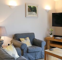 A living room with grey armchairs, a sofa, a lamp, a wooden coffee table, a TV on a wooden stand, and a framed picture on the wall at Tarn Lodge in Bowness-On-Windermere