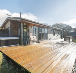 A wooden deck with chairs and a hot tub outside a wooden house at Tarn Lodge in Bowness-On-Windermere