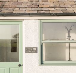A mint green door and window on a white exterior wall with a coat rack visible inside at Ty ar Ben Bryn in Pencarnisiog near Rhosneigr