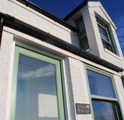 Exterior of a white textured building with green window frames and a black drainpipe at Ty ar Ben Bryn in Pencarnisiog near Rhosneigr