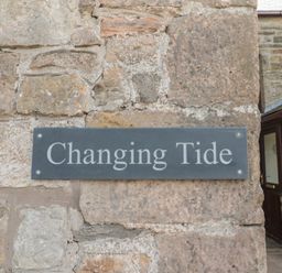 A stone wall with a sign reading Changing Tide at Changing Tide in Beadnell