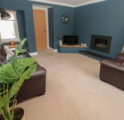 A living room with brown leather sofas a TV on a corner shelf and a fireplace at Changing Tide in Beadnell