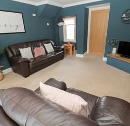 A living room with two brown leather sofas a wall mounted tv a plant and a door at Changing Tide in Beadnell