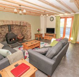 A living room with two gray sofas a wooden coffee table stone fireplace and glass doors with green curtains at Little Brook Cottage in Laugharne