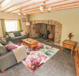 A living room with two sofas a coffee table a wood stove and a television at Little Brook Cottage in Laugharne