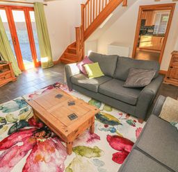 A living room with two gray sofas a wooden coffee table a floral rug a wooden cabinet a TV on a wooden stand and stairs leading upstairs at Little Brook Cottage in Laugharne