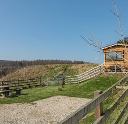 A small wooden cabin with a bench outside surrounded by a wooden fence and grass at Castle View Cabin in Cloughton