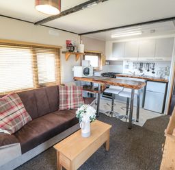 A small living area with a sofa and kitchen with bar stools and a wooden coffee table at Castle View Cabin in Cloughton