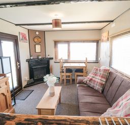 A living room with a brown sofa, wooden coffee table, dining table with chairs, fireplace, and wooden cabinet at Castle View Cabin in Cloughton