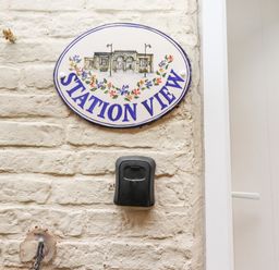 A white brick wall with a ceramic house name plaque reading Station View and a black doorbell at Station View in Whitby