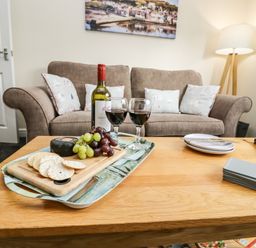 A living room with a brown sofa pillows a floor lamp and a wooden coffee table with wine grapes crackers and a cutting board at Station View in Whitby
