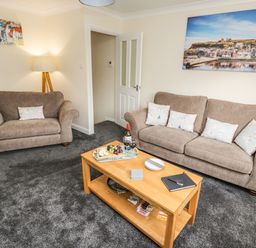 A living room with two sofas a wooden coffee table with snacks and wine and wall art at Station View in Whitby