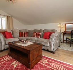 A living room with a grey sectional sofa with red and striped cushions a wooden coffee table and a desk with a chair at Scenic Views in High Bickington