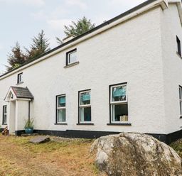 A white two-story house with multiple windows and a front porch surrounded by trees and grass at Kealduff Lower in Glenbeigh County Kerry