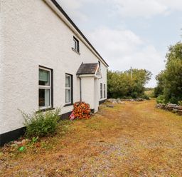 A white house with black trim next to a dirt driveway and trees at Kealduff Lower in Glenbeigh County Kerry