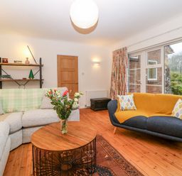 A living room with two sofas a wooden coffee table with flowers a wooden floor and a window showing a garden at Casalmare in Exmouth