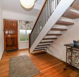 An entryway with a wooden front door a window with a patterned shade a staircase with carpeted steps a rug on a wooden floor and a black metal table at Casalmare in Exmouth
